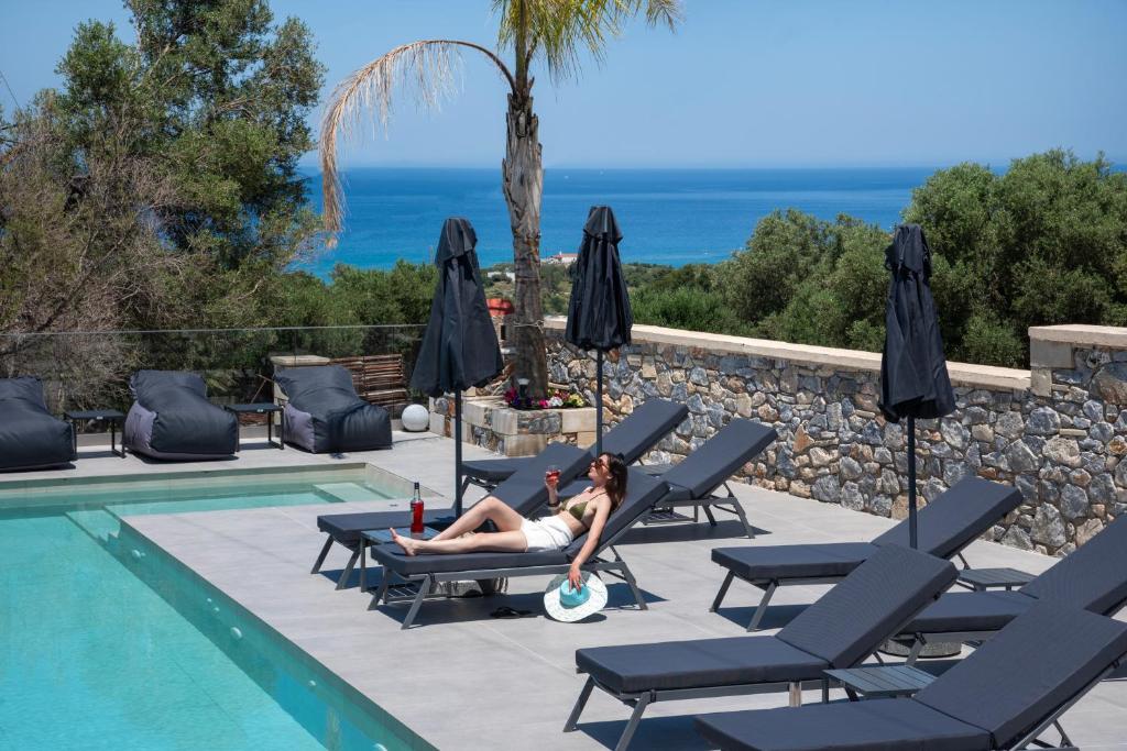 a woman laying on lounge chairs next to a swimming pool at Villa Manel in Georgioupoli