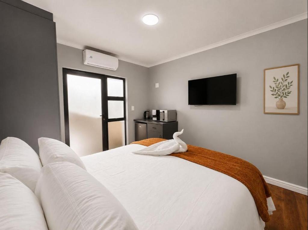 a bedroom with a white bed with a tv on the wall at Pecan Tree Lodge in Cape Town