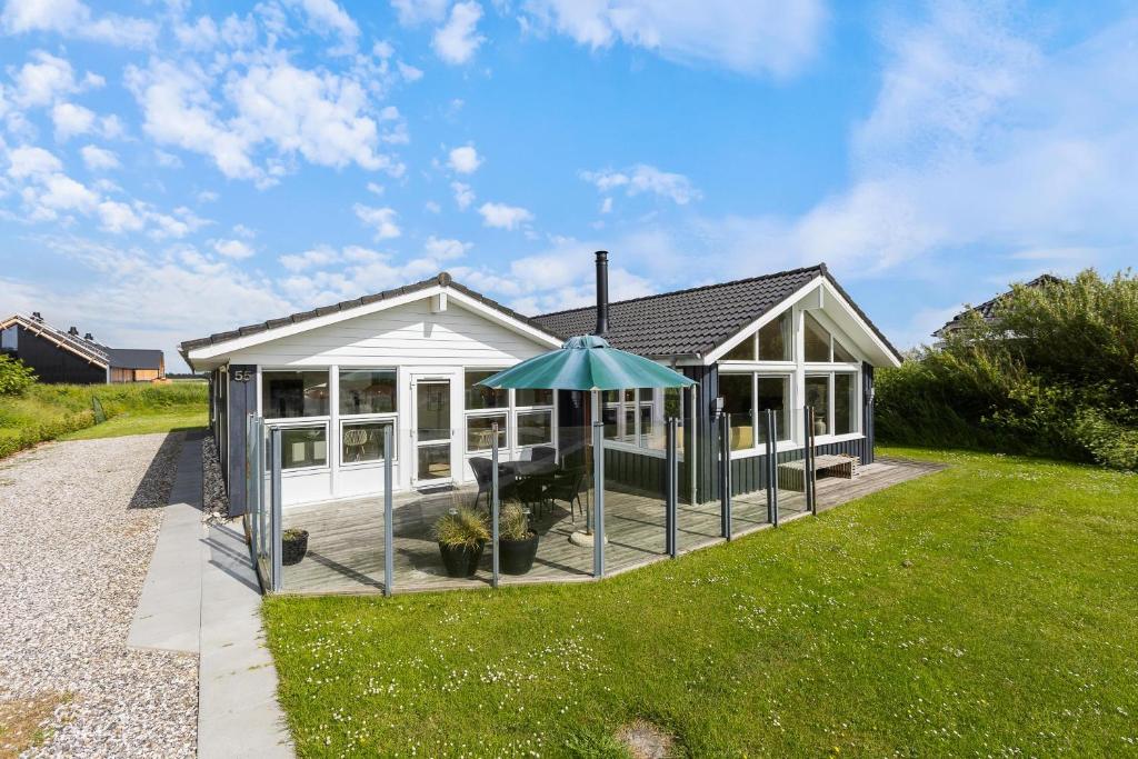 a small white house with an umbrella in the yard at Feriehus 1120 in Ringkøbing