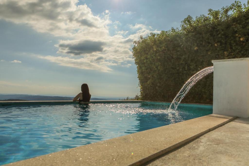 a person laying in a swimming pool with a fountain at Casas do Soito in Seia
