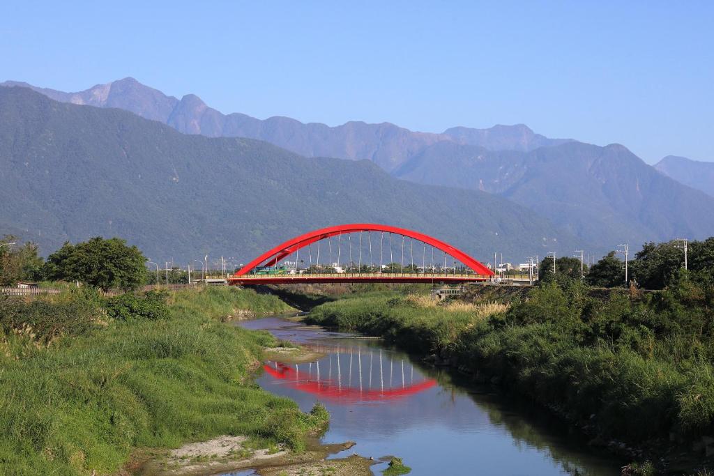 eine rote Brücke über einen Fluss mit Bergen im Hintergrund in der Unterkunft Bridge Bed and Breakfast in Hualien