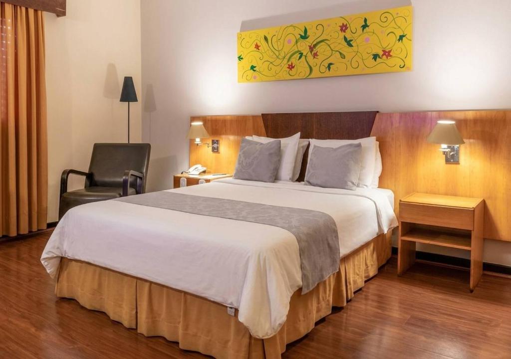 a hotel room with a large bed and a chair at Dexter Hotel - Volta Redonda in Volta Redonda