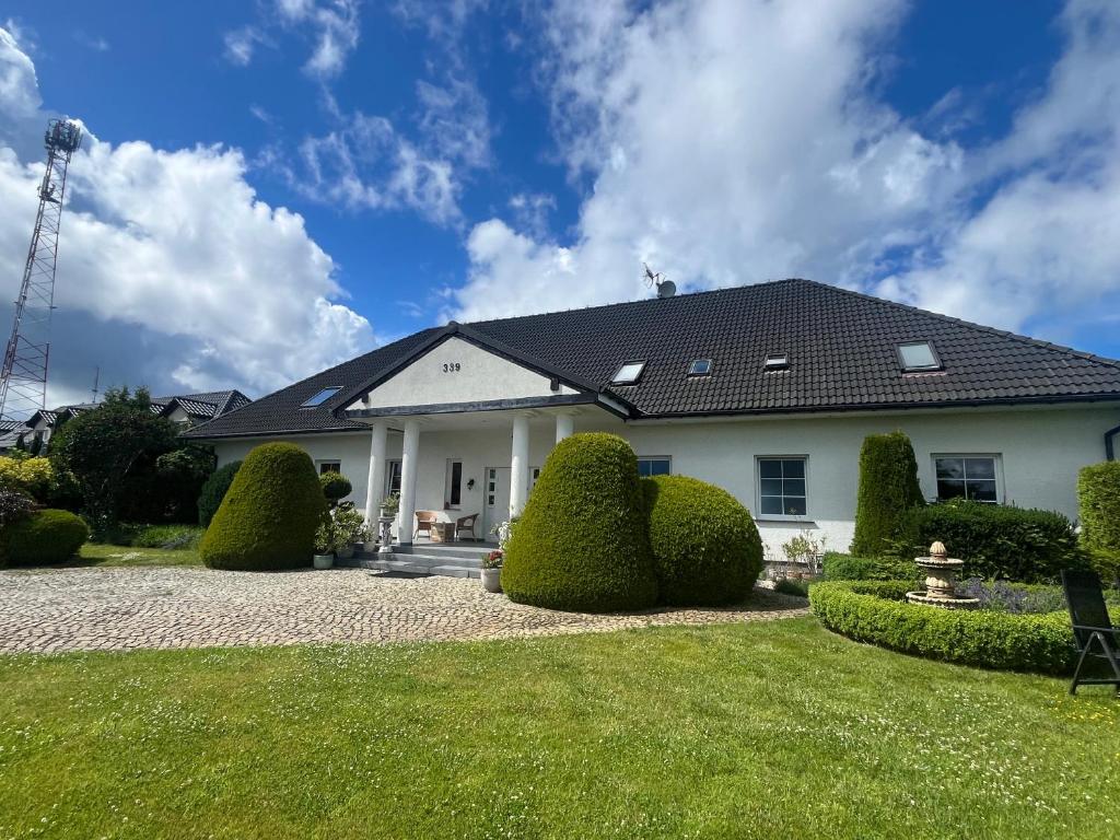 a white house with a black roof and some bushes at Dworek na Polance in Wrzosowo