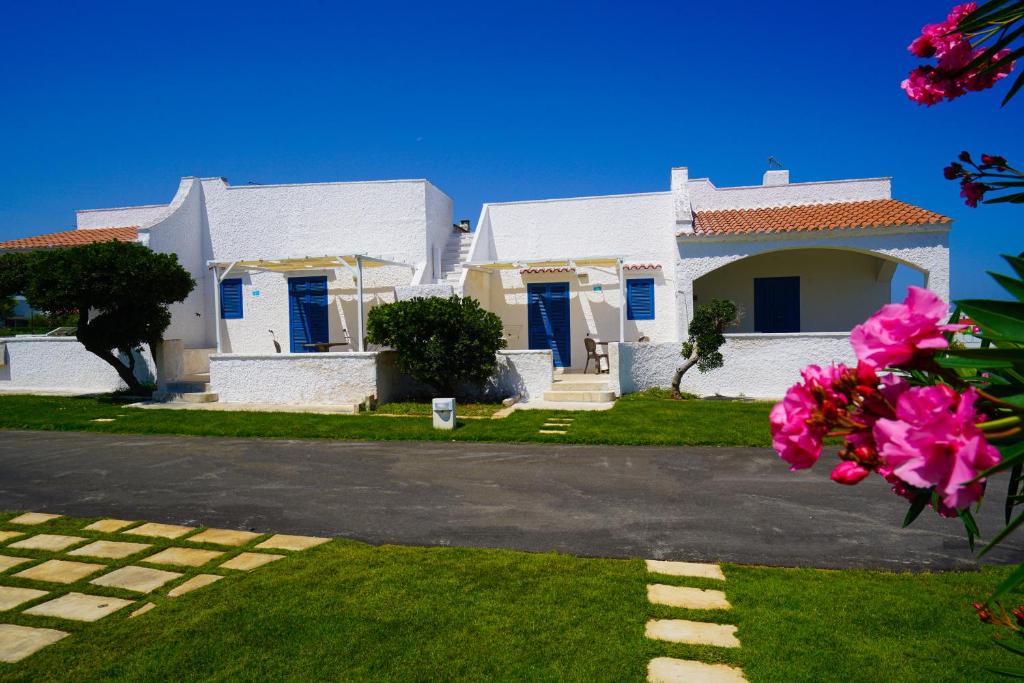 a white house with blue doors and pink flowers at Mapo Village Plaia in Villanova di Ostuni