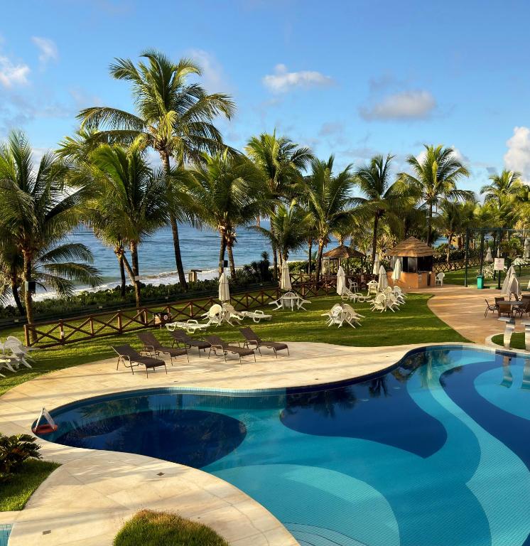 a pool at a resort with palm trees and the ocean at Flat 3 Quartos Pé na Areia, Piscina e Mar, Summer House Genipabu, Guarajuba in Guarajuba