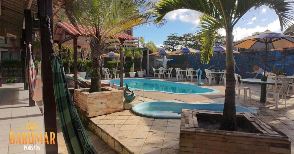 a swimming pool with palm trees and tables and chairs at Pousada Barumar in Lucena