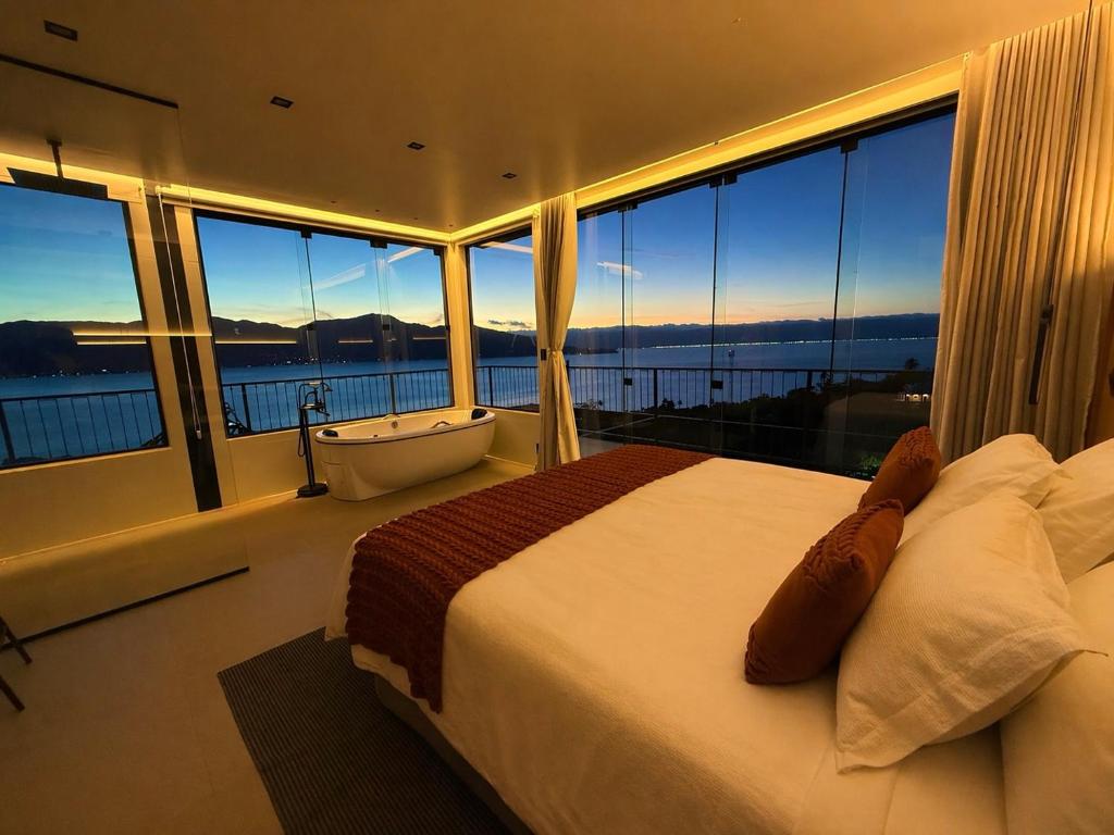 a bedroom with a large bed and a tub and windows at Casa Gaia GuestHouse in Ilhabela