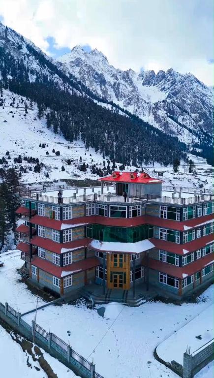 a building in the snow with mountains in the background at Gems Palace Hotel Naltar in Jugut