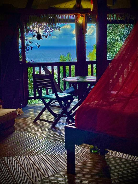 a porch with a table and a hammock and the ocean at Hutte Karaib Reve de Robinson Une cabane perchee au cœur de la nature tropicale vue mer in Terre-de-Bas