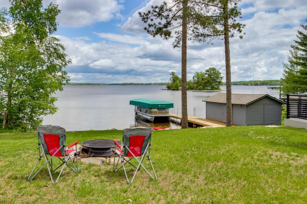 two chairs and a grill on a lawn next to a lake at Lakefront Northwoods Cabin w/ Shared Dock & Views! in Tower