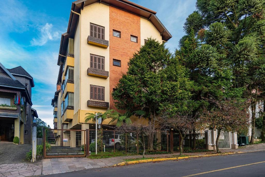 a tall building with trees in front of a street at Rosa Condomínio Vale azul in Gramado