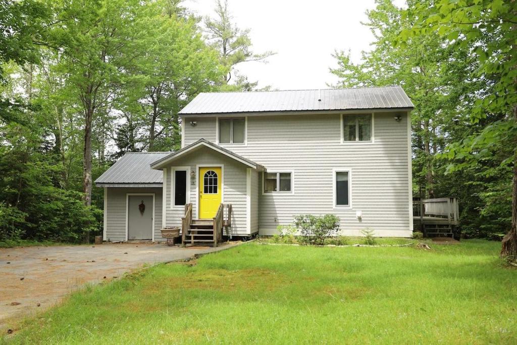 a white house with a yellow door in a yard at Goose Hollow 19 Estates Pet Friendly Private Waterfront Home in Campton