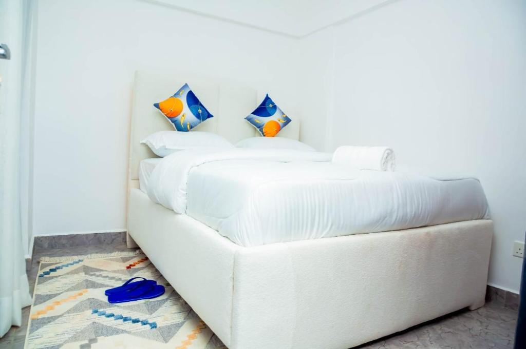 a white bed with white sheets and blue shoes on the floor at AJHOMESKisumu in Kisumu