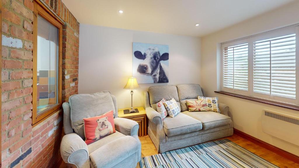 a living room with two chairs and a cow picture on the wall at The Byre in Banbury