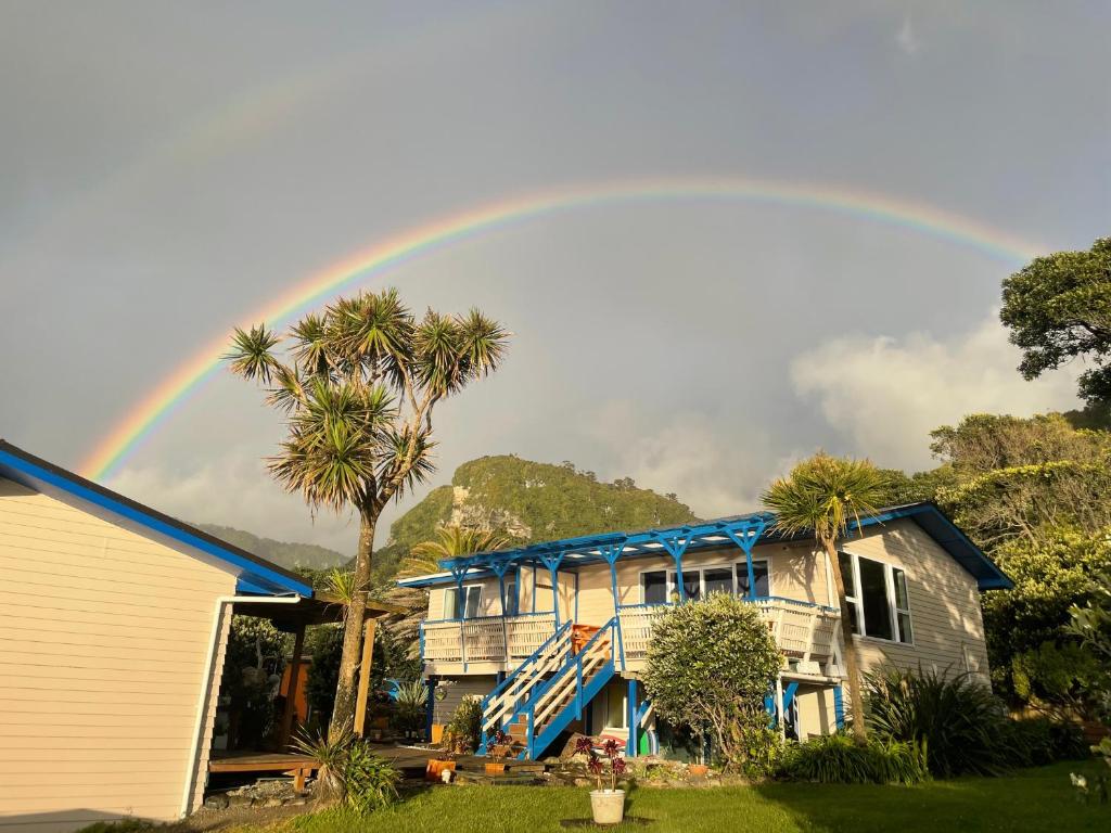 a rainbow over a house with a palm tree at Punakaiki Beach Hostel in Punakaiki