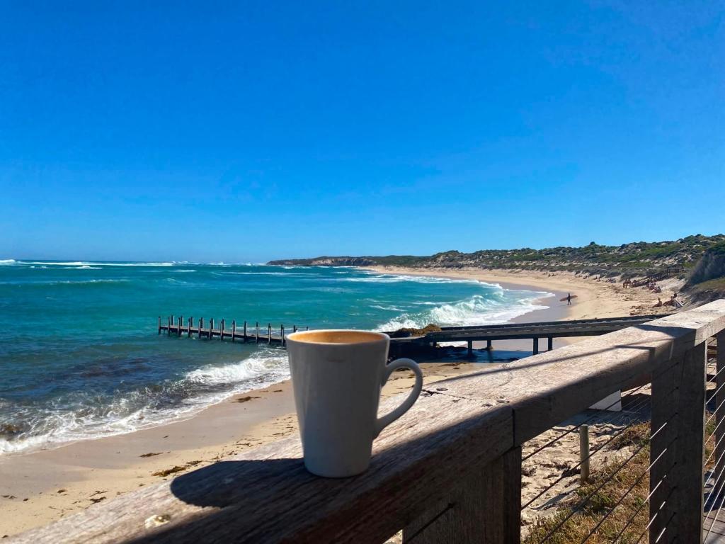 a cup of coffee sitting on a fence near the beach at Beach Studio with Ocean View in Gnarabup