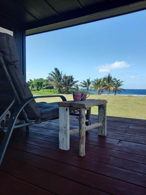 a table and a chair on a deck with a view of the ocean at Kuki Beach Bach in Rarotonga