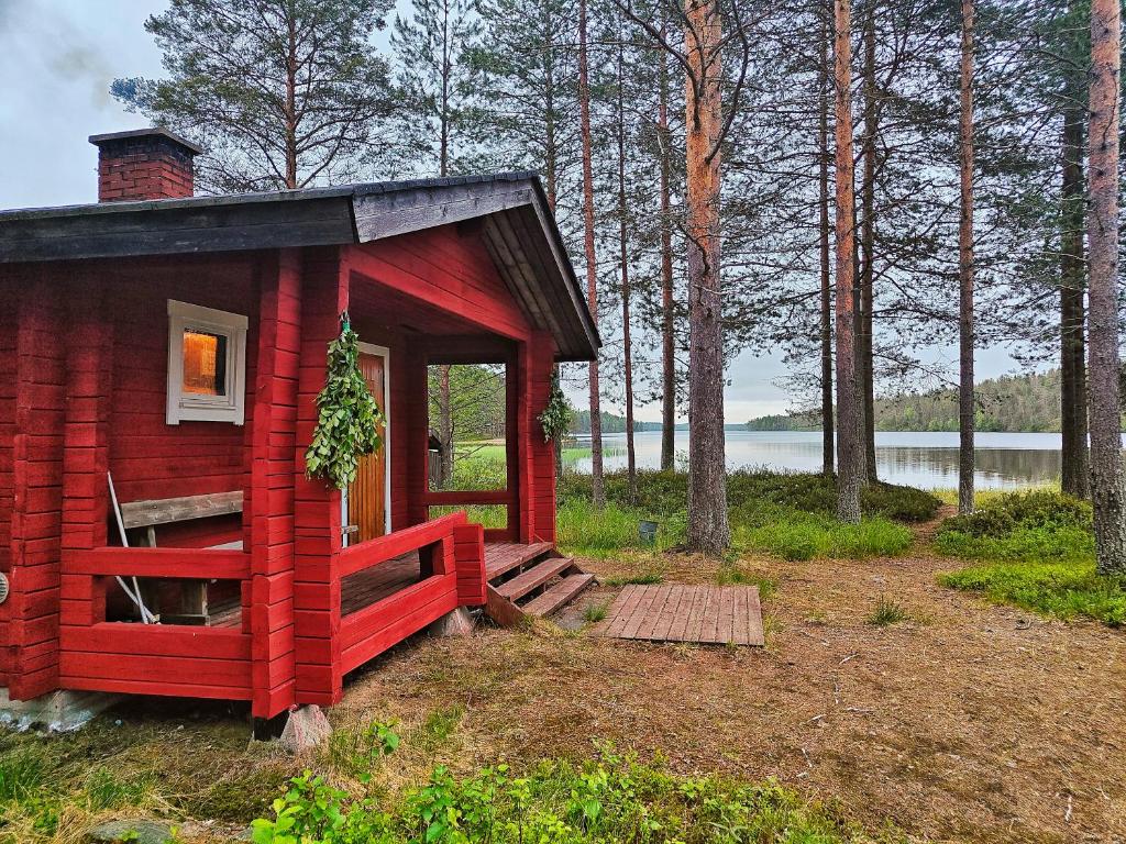 a red tiny house in the woods with a lake at Hossa Teeriranta in Teeriranta