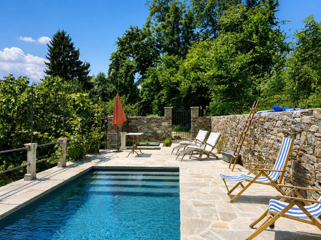 a swimming pool with chairs and a table next to a stone wall at Corte Villa Donati in Cissano