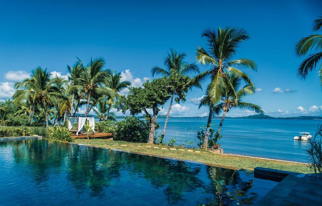 a swimming pool with palm trees and the ocean at Belamandy Lodge Hotel au luxe simple in Anjramarango