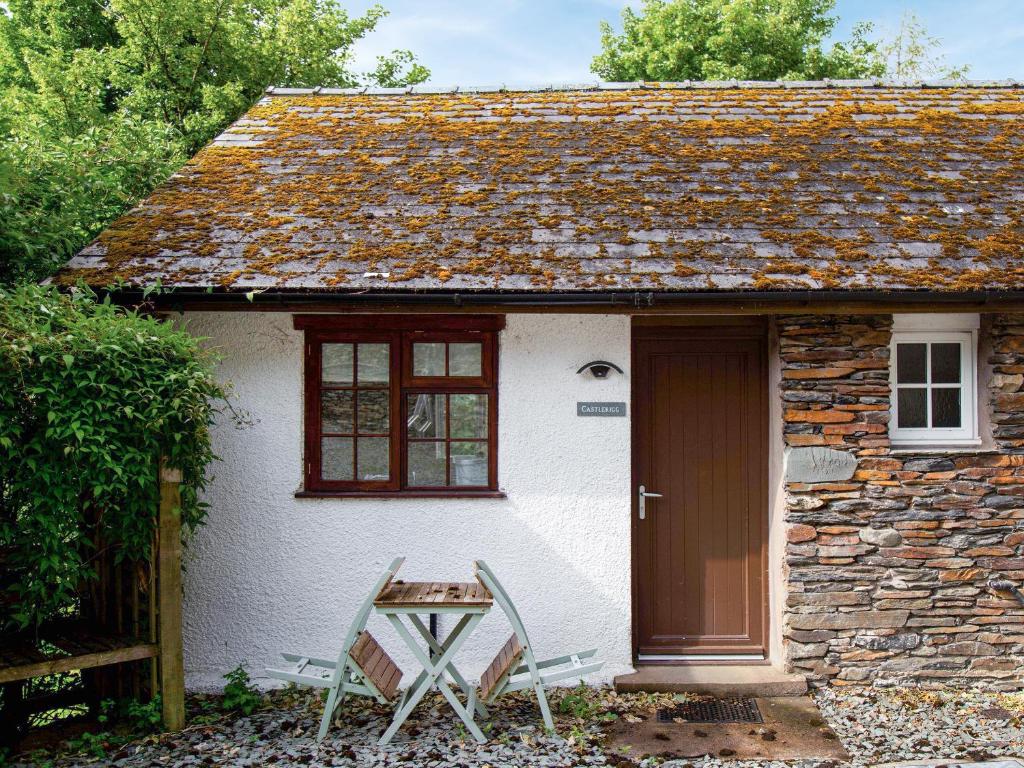a small white cottage with a door and two chairs at Castleriggs Cottage - Uk45178 in Threlkeld