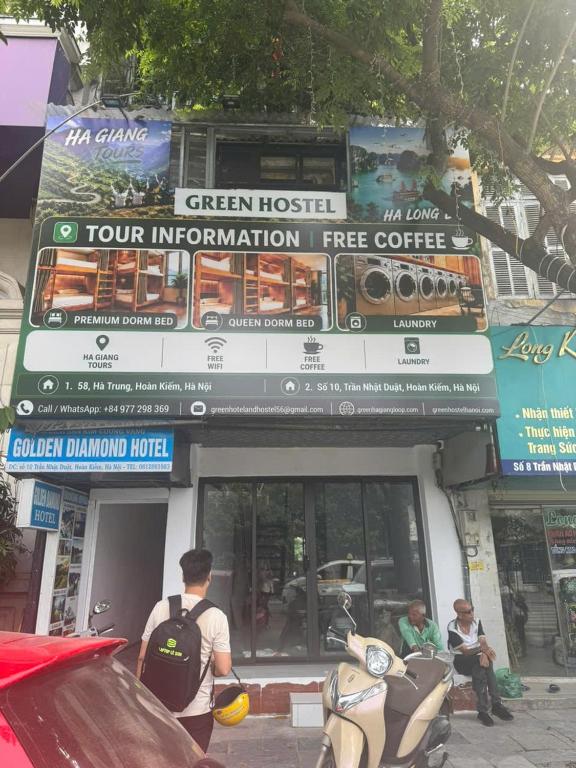 a man standing in front of a green hotel with a sign at Green Hostel Hanoi 2 in Hanoi