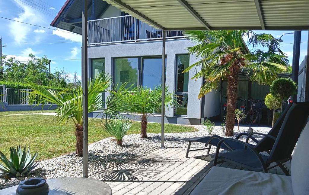 a patio with chairs and palm trees and a house at Kikapcs apartman in Alsóörs