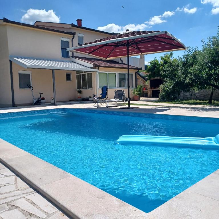 a swimming pool with an umbrella and a house at Apartman Katić - Rental Home in Stolac