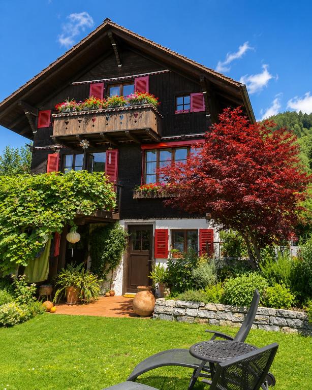 a house with red shuttered windows and a table at "Mon Rêve" Nature, Tranquility & Lake Thun in Sigriswil
