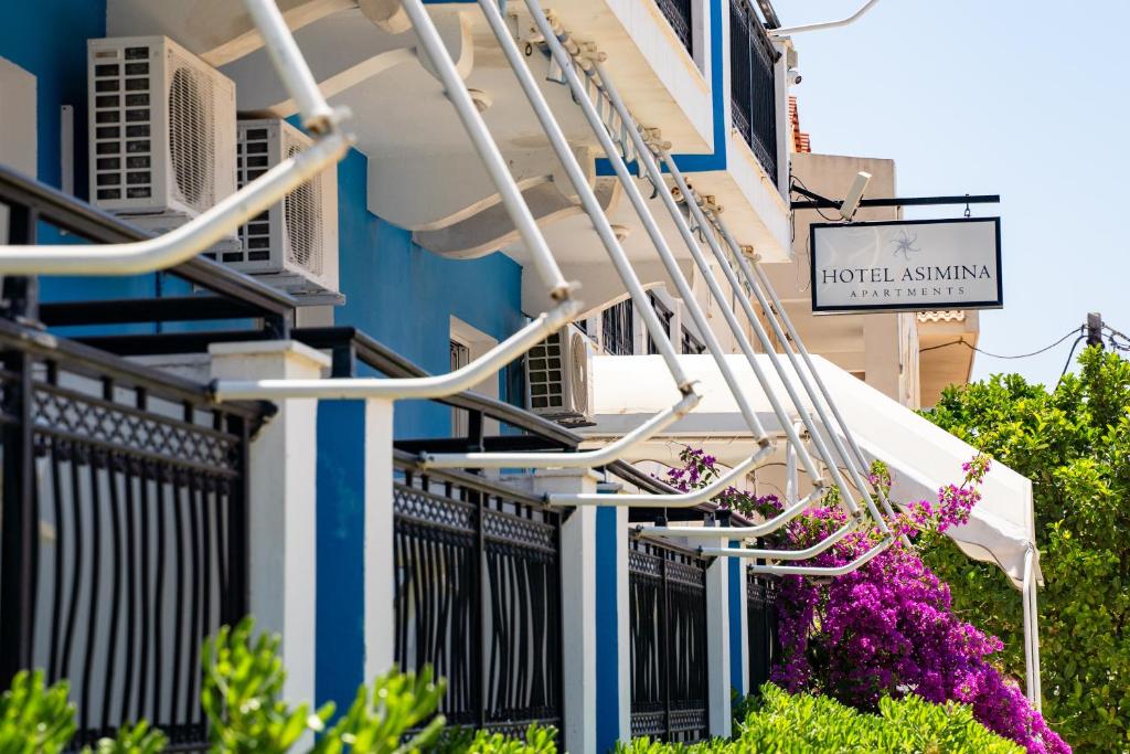 a building with a hotel assay sign and purple flowers at Hotel Asimina Laganas in Laganas