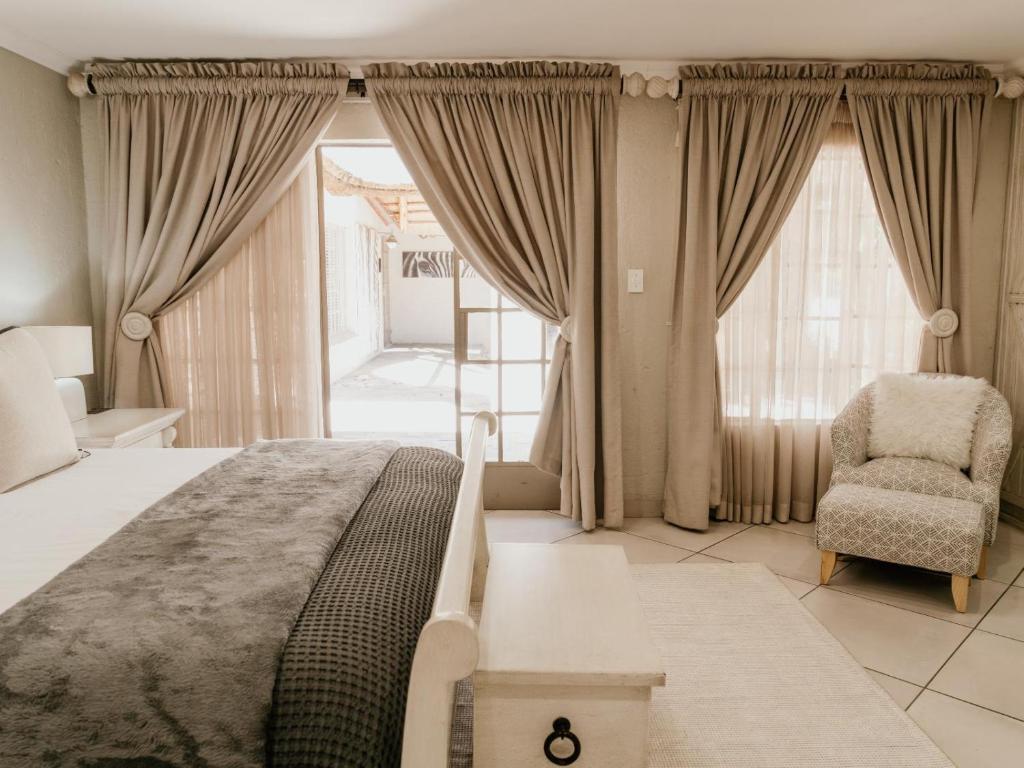 a bedroom with a bed and a chair and windows at Decollage Estate in Polokwane