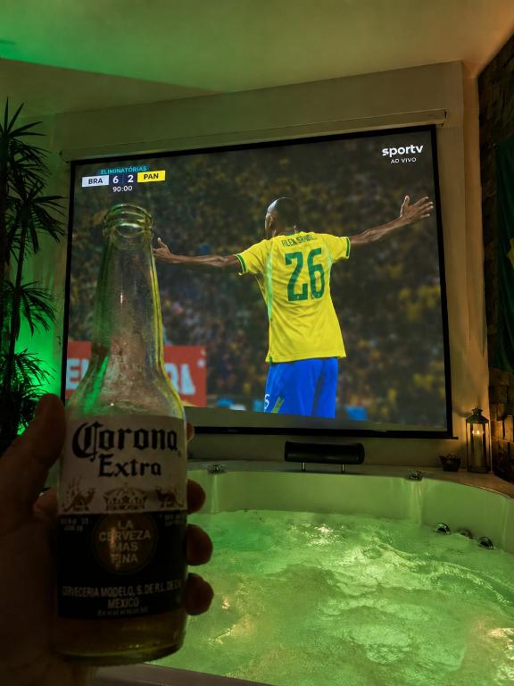 a person holding a bottle of corona beer in front of a television at Aconchego Valença & Spa in Nova Friburgo