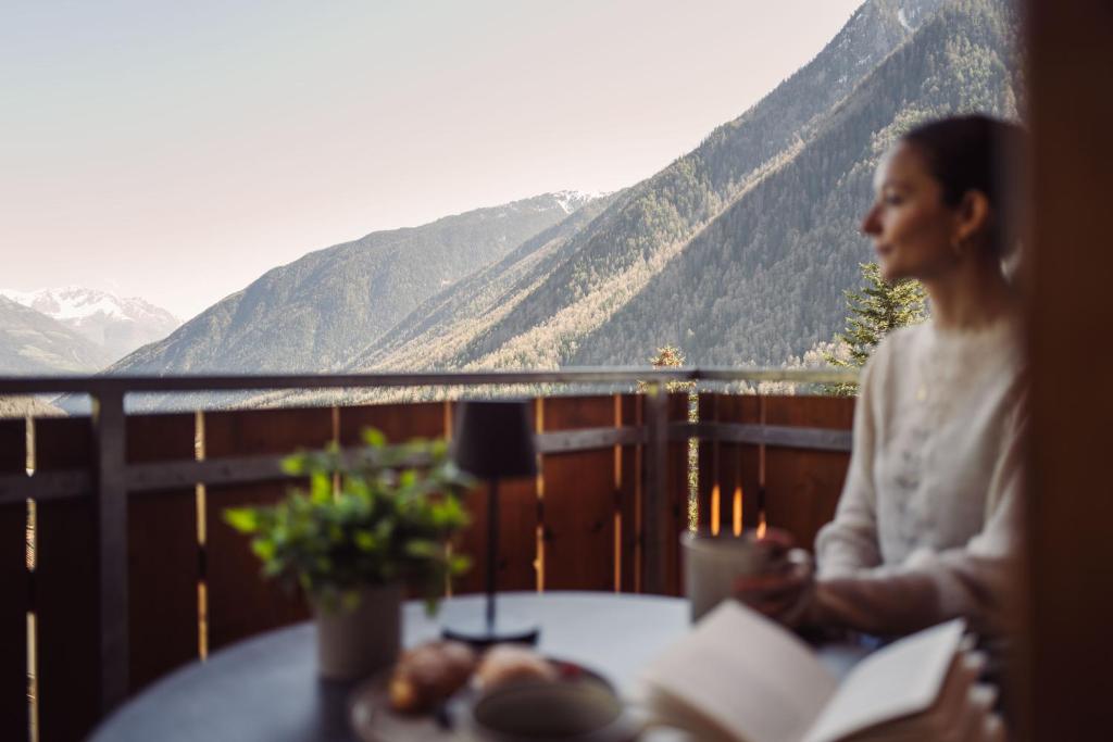 a woman sitting at a table with a view of mountains at Das Bergfrieden Nature Active Hotel in Martello