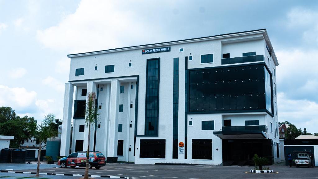 a white building with a car parked in a parking lot at Ocean Front Hotels Enugu in Awkuzu