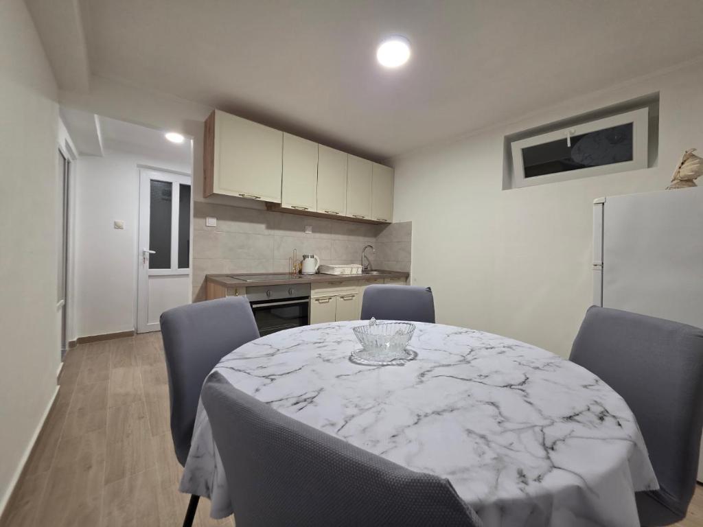 a dining room table with chairs and a kitchen with a refrigerator at Garden Terrace Apartment in Igalo