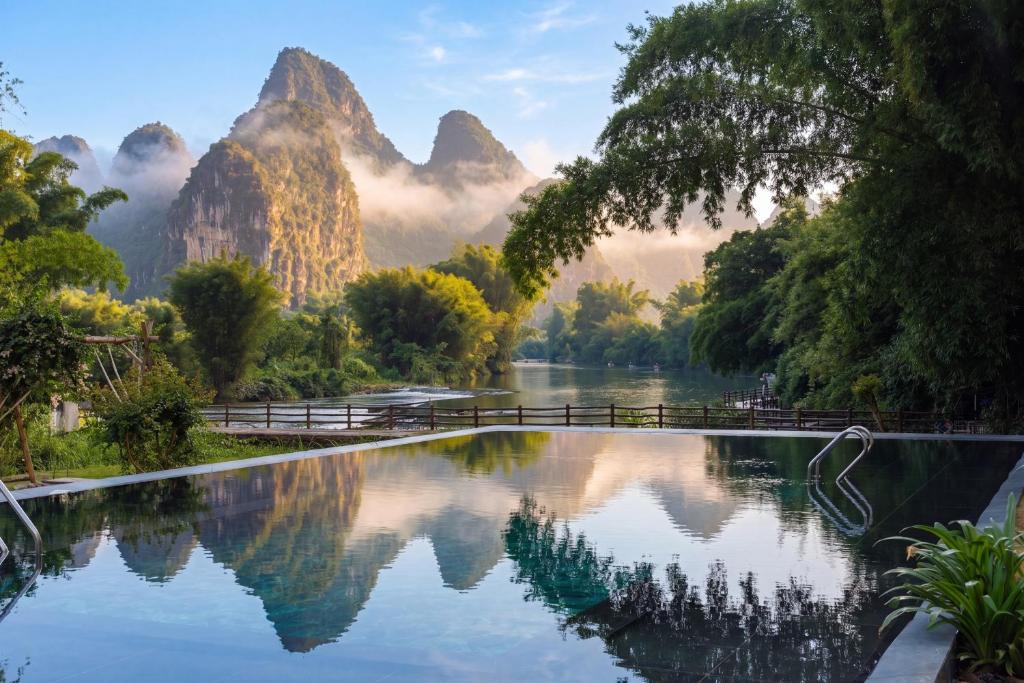 a pool of water with mountains in the background at L'Eau Vive de Qixi Meidi - Riverfront Infinity Pool & Log Cabin Cafe - Outdoor Cooking Class - Complimentary Shuttle within 8 Kilometers in Yangshuo