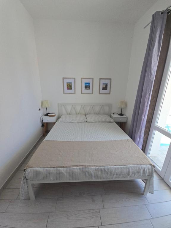 a white bedroom with a large bed with two tables at camera con terrazza vicino al mare e pineta in Follonica