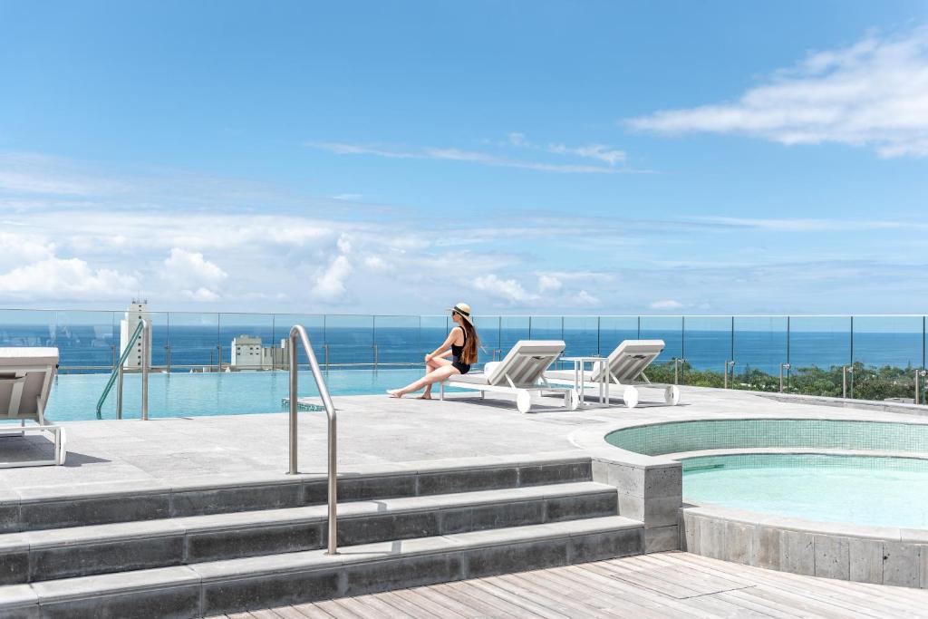 a woman sitting on a chair next to a swimming pool at Doubletree By Hilton Lagoa Azores in Lagoa