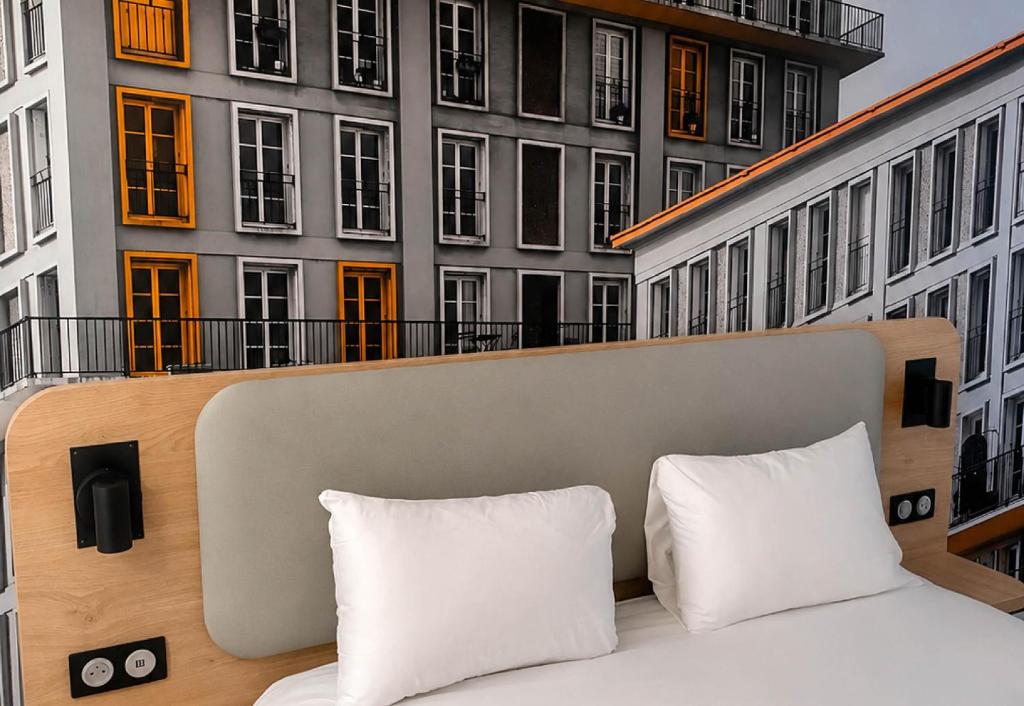 a bed with two pillows on a balcony with buildings at B&B HOTEL Le Havre Centre in Le Havre