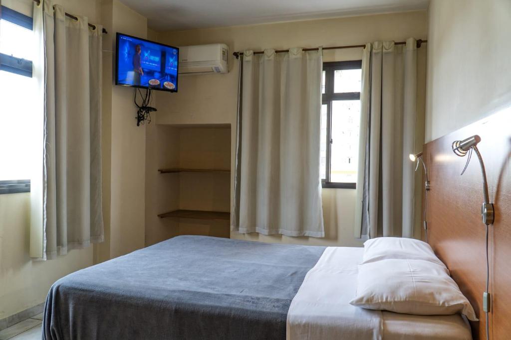 a bedroom with a bed and a tv on the wall at Hotel Vila Rica Flat in Resende
