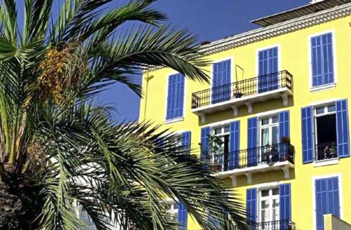a yellow building with palm trees in front of it at Chambres d'hôtes Le Regent in Hyères