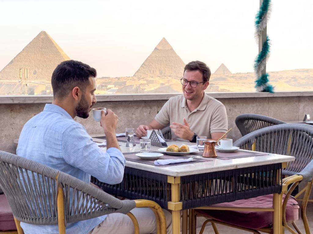 two men sitting at a table in front of the pyramids at Luxurious GEM and PYRAMIDS view in Cairo