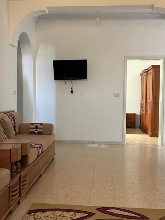 a living room with a couch and a tv on a wall at Résidence El hechene in Ḩawmat al Ḩashshān