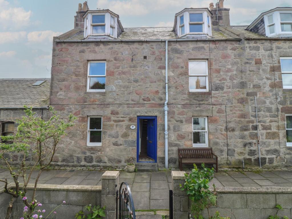 an old stone house with a blue door and a bench at Footdee Cottage in Aberdeen