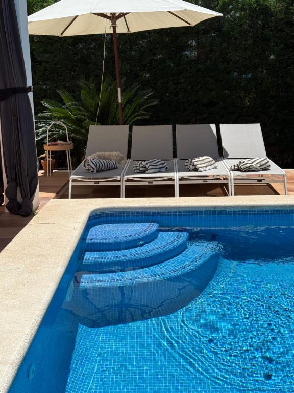 a swimming pool with chairs and an umbrella next to it at Villa Ferrera Select A in Cala Ferrera