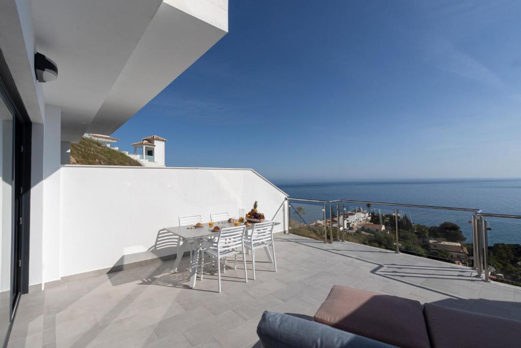 a balcony with a table and chairs and the ocean at NerjaPlus Terraza de Ladera Apartamento V11 in Nerja