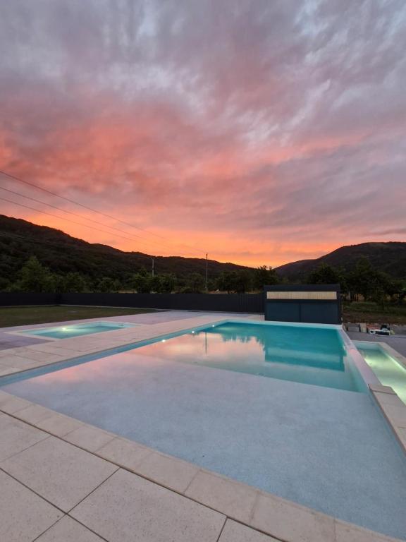 a large swimming pool with a sunset in the background at Transalpina Retreat in Novaci-Străini