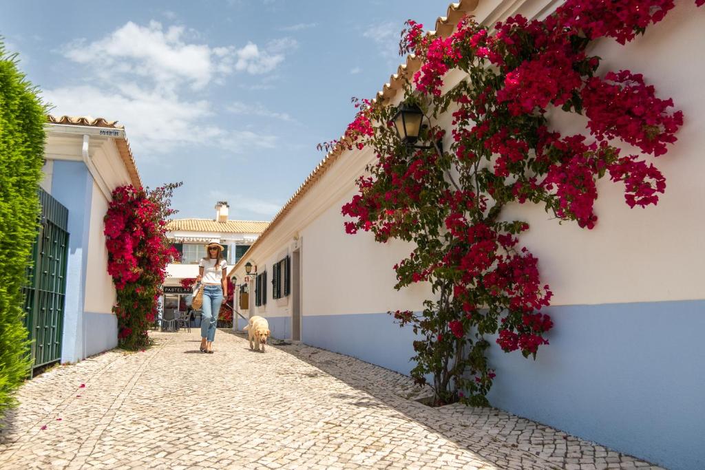 a woman walking her dog down a street with flowers at Vila Bicuda Resort in Cascais