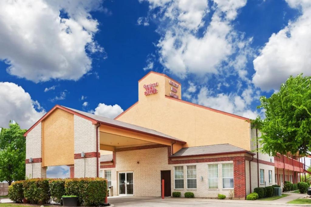 a building in front of a blue sky with clouds at Garland Inn & Suites near Dallas TX in Garland