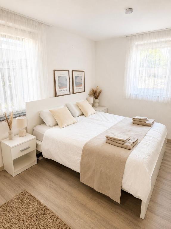 a white bedroom with two beds and two windows at STAY - Comfort Apartment in Friedrichshafen